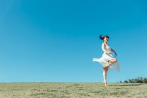 青空と草原の中バレエをする女性